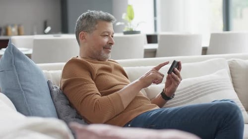 Mature Man Using Smartphone While Relaxing on Living Room Sofa