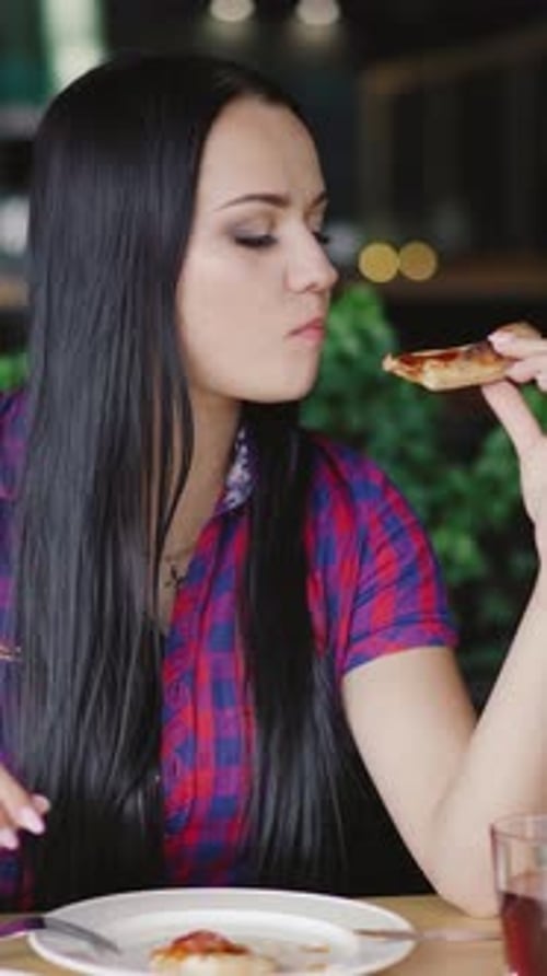 beautiful girl in a plaid shirt is eating a slice of pizza at a table in the pizzeria.