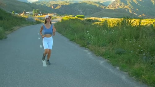 Fit Woman Runs Confidently Along a Road with Mountain Slopes Behind