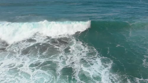 An interesting aerial birds eye view shot following a wave crashing into shore as the white wash swi
