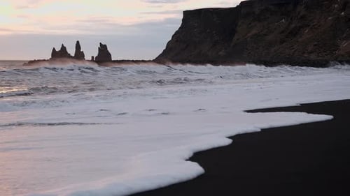 Waves crash on an Icelandic black sand beach in Vik Iceland. The sunset shines around basalt cliffs