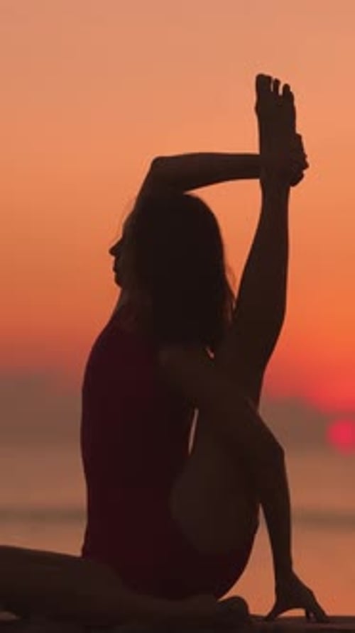 Woman Silhouetted Practicing Yoga Stretch Pose at Sunrise on Beach