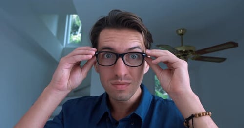 Porträt eines 30-jährigen jungen Mannes in einem blauen Hemd, der eine Brille aufsetzt, um besser zu sehen, und lächelt