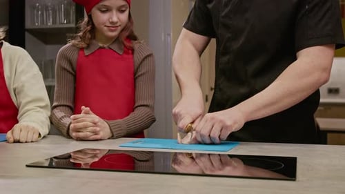 Männlicher Koch bringt Mädchen im Kochkurs das Schneiden von Hühnchen bei