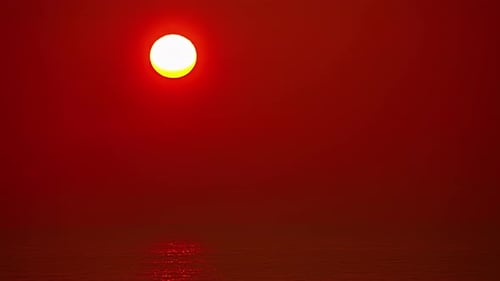An orange, glowing sun rises over the ocean water on a foggy day - time lapse