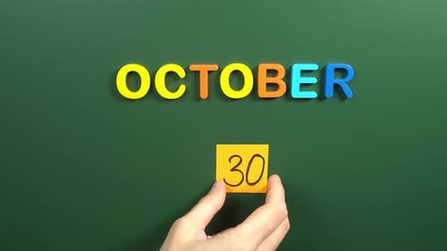 Hand sticking a sticker 30 October calendar day on school board. 30 date of October. Thirtieth day