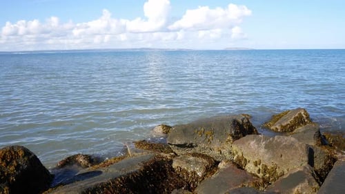 Sunny blue ocean horizon over stone pebble beach coastline clear holiday scene