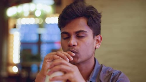 Young Man Seated Indoors Sipping Drink Through Straw