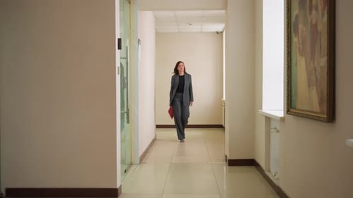 Businesswoman Walking Through Office Hallway with Folder in Hand