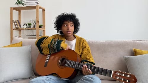 Young Woman Plays Guitar on Sofa Indoors