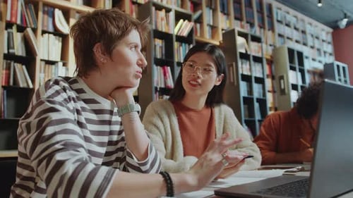 Female University Students Discussing Homework on Laptop in Library