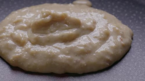 Extreme close-up of pouring pancake batter on a hot pan.