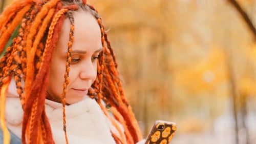 Beautiful Young Woman with Dreadlocks Using Smartphone in Autumn Park
