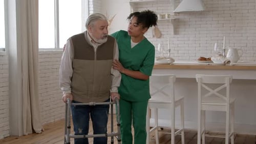 African American Female Caregiver Assisting Elderly Man in Using Walking Frame