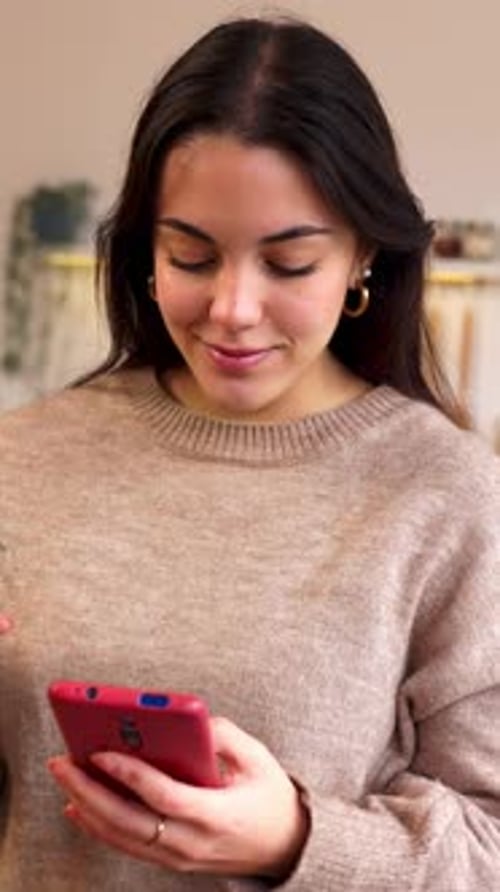 Smiling Woman Uses Smartphone Indoors