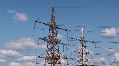 Two high-voltage transmission towers and power lines against a bright blue sky with scattered