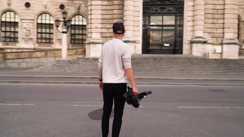 A rotating shot of a young filmmaker holding a heavy camera in an old city.