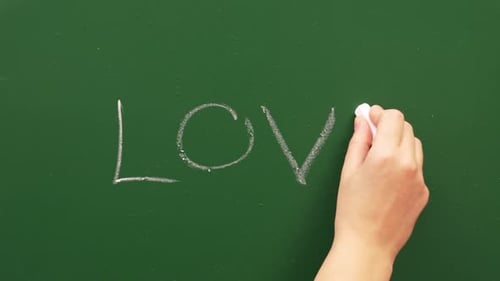 A Hand Writes Love On A Green Chalkboard