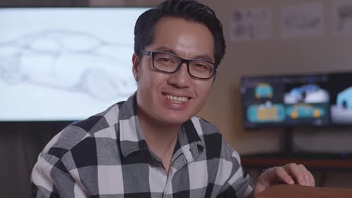 Asian Man Automotive Designer Smiling To The Camera While Working On The Sculpture Of Car Clay