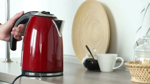 Person places red kettle on stand, prepares tea
