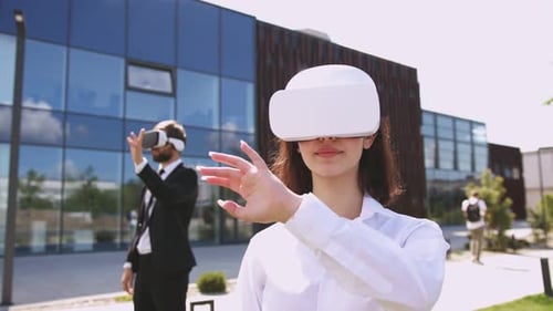 Young Attractive Businesswoman in VR Headset Making Swiping Gesture While Her Male Colleague Using
