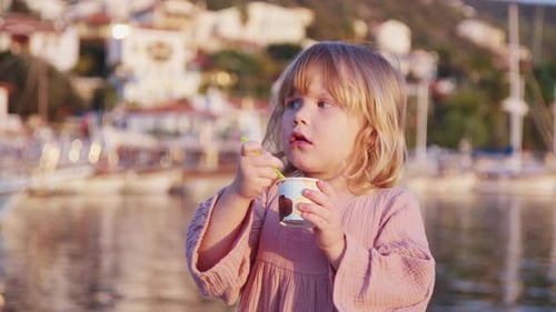 Cute Blonde Girl Eats Ice Cream on Street From a Plastic Jar