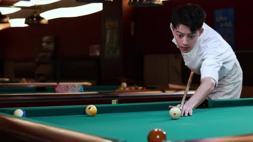 Young pool player hit the white cue ball with the cue to drives brown american pool ball into the po