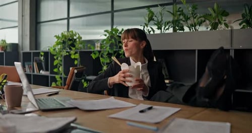Businesswoman Eating Noodles at Desk in Modern Office