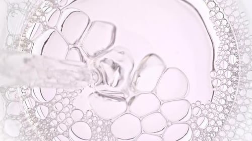 Des bulles d'air transparentes sortent d'une pipette de laboratoire et éclatent à la surface d'un liquide clair à Petri