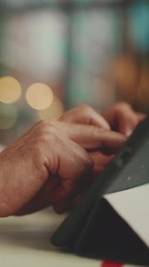 Close-up das mãos de um empresário maduro trabalhando no tablet sentado no café ao ar livre