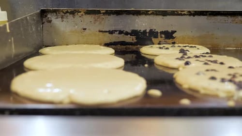 Buttermilk and chocolate chip pancakes sizzle on flattop grill, slider // 4K