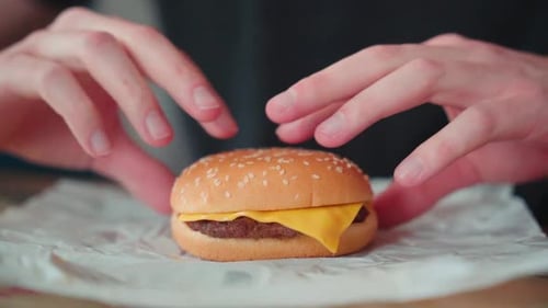 Slow motion young caucasian man bites into burger at home, cheeseburger eating enjoyment, close up p