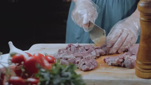 Gloved Hands Chopping Meat with Knife on Board