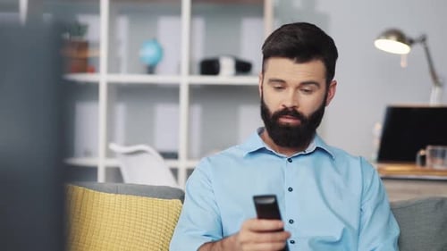 A Man is Comfortably Relaxing in His Home Enjoying Some TV While Using a Remote Control