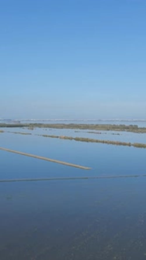 Luftdrohne über überflutete landwirtschaftliche Felder neben einem Dorf mit Blick auf den blauen Himmel in der