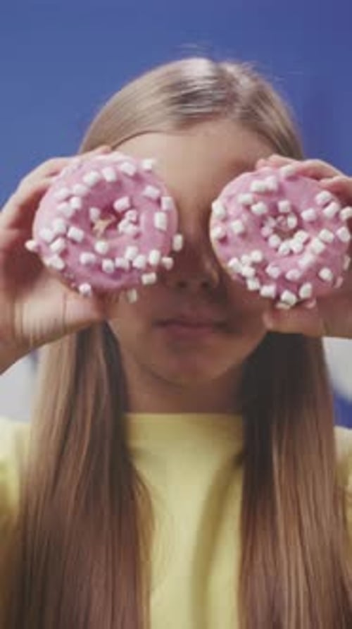 Smiling Girl Poses with Donuts in Front of Eyes