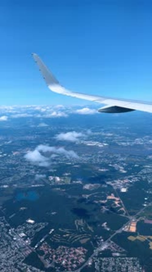 Aerial view of aircraft wing flying over landscape and clouds.