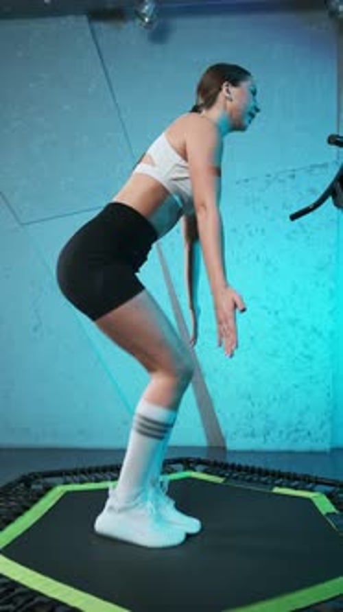 Joven enérgica chica de fitness con top blanco y pantalones cortos negros haciendo ejercicios saltando en el móvil mini tr