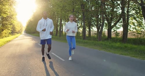 Cheerful Young Caucasian Beautiful Woman and African American Handsome Man Running Outdoors in Park