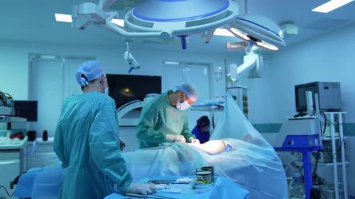 Doctors in medical uniform perform a surgical procedure for removing fat.