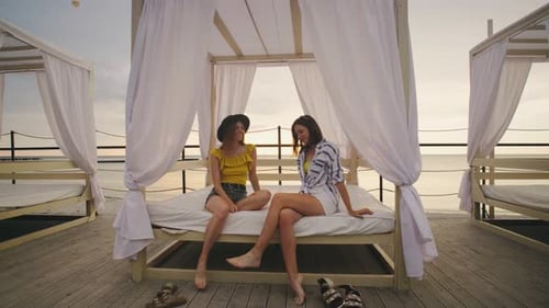 Two Women Relaxing on Beach Beds By the Serene Seaside Enjoying the Sunset View
