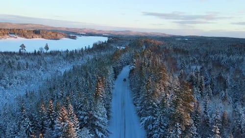 Aerial of a car driving down a snowy road in the middle of winter