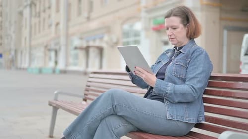 Woman Using Tablet on Bench in Urban Setting