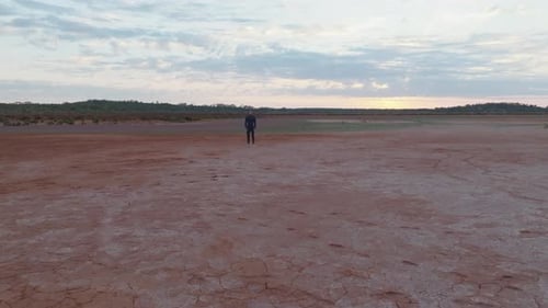 Drone clip moving towards male model with dark hair wearing wetsuit, stood still in red desert lands