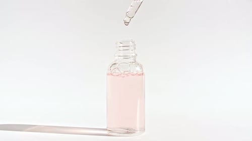 Dropper Adding Pink Liquid to Glass Cosmetic Bottle