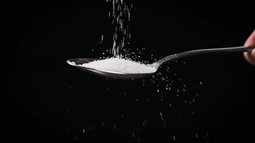 Sugar Falls Into Spoon on Black Background Slow Motion CloseUp Copy Space