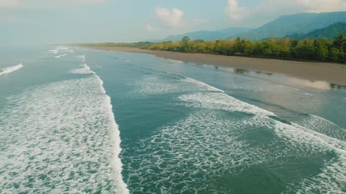 Wide aerial view of Playa Linda beach with calm waves and lush trees in Costa Rica