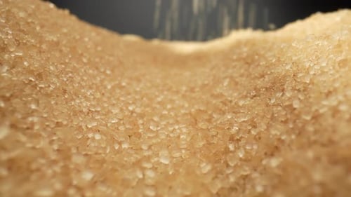 Golden brown sugar delicately cascading onto a sleek black background