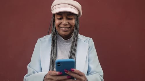 Stylish Woman Using Cell Phone Against Red Wall