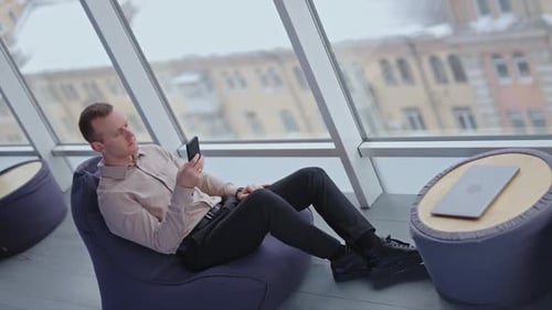 Young Adult Relaxing on Beanbag Chair Using Phone